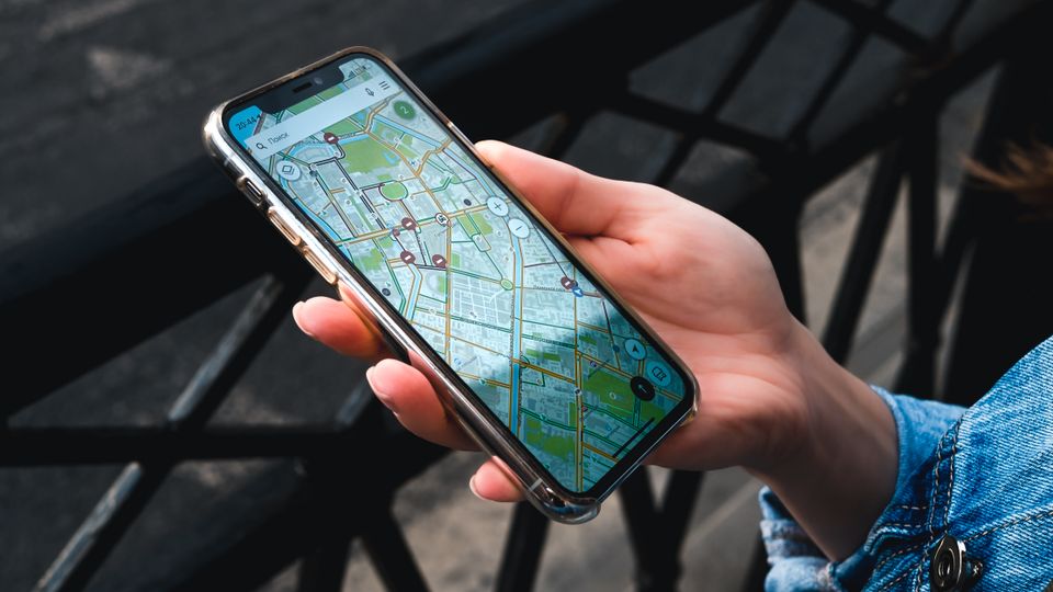 Mão segurando um celular com um aplicativo de mapa aberto ao ar livre.