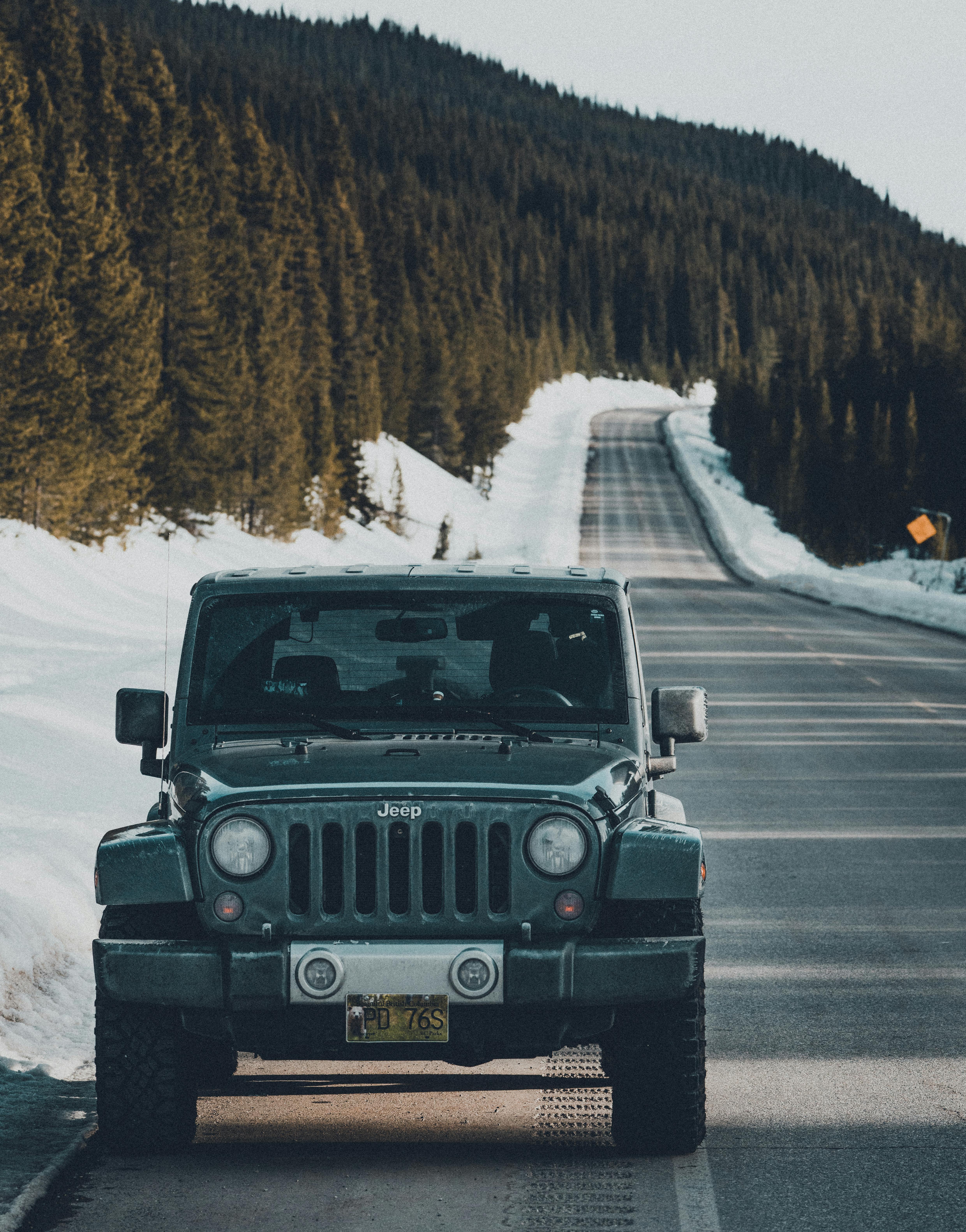 Free A rugged SUV parked on a snowy mountain road lined with tall pine trees. Stock Photo
