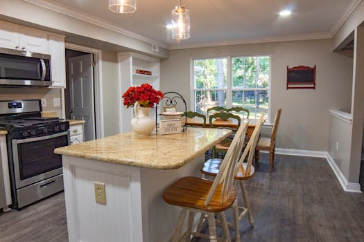 Cozy kitchen interior featuring a granite island, chairs, and natural light.