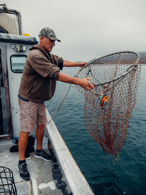 A Man Holding a Fish Net on a Boat · Free Stock Photo