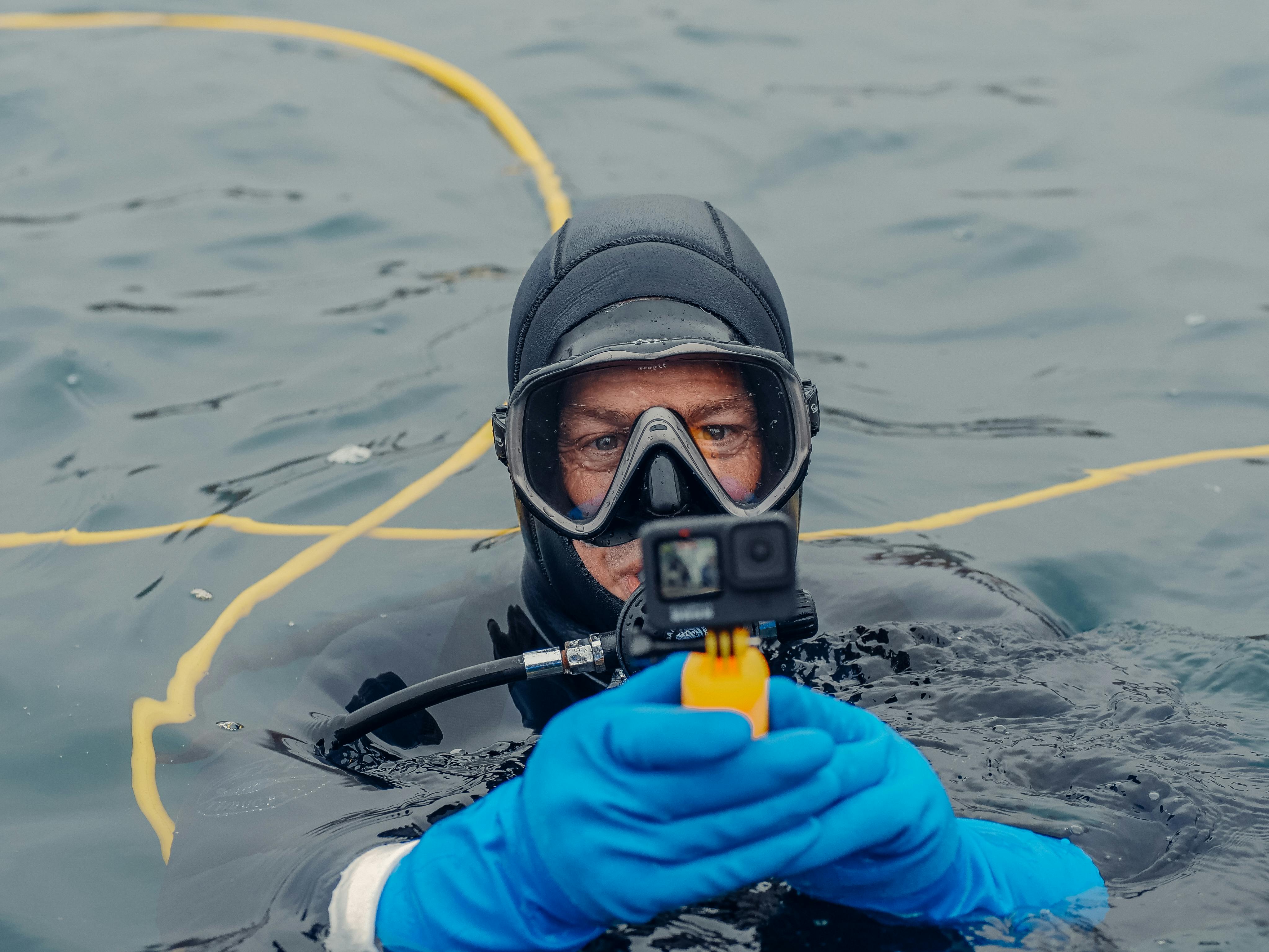A scuba diver in blue gloves records underwater using a camera in open water.