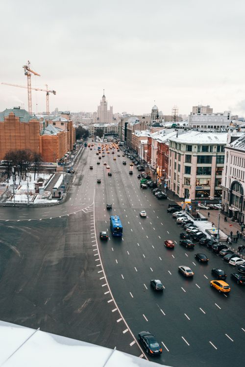 Free A bustling city street view with vehicles and construction cranes, surrounded by snowy buildings. Stock Photo