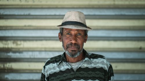 Free Portrait of an elderly man in a fedora standing against a metallic background. Stock Photo