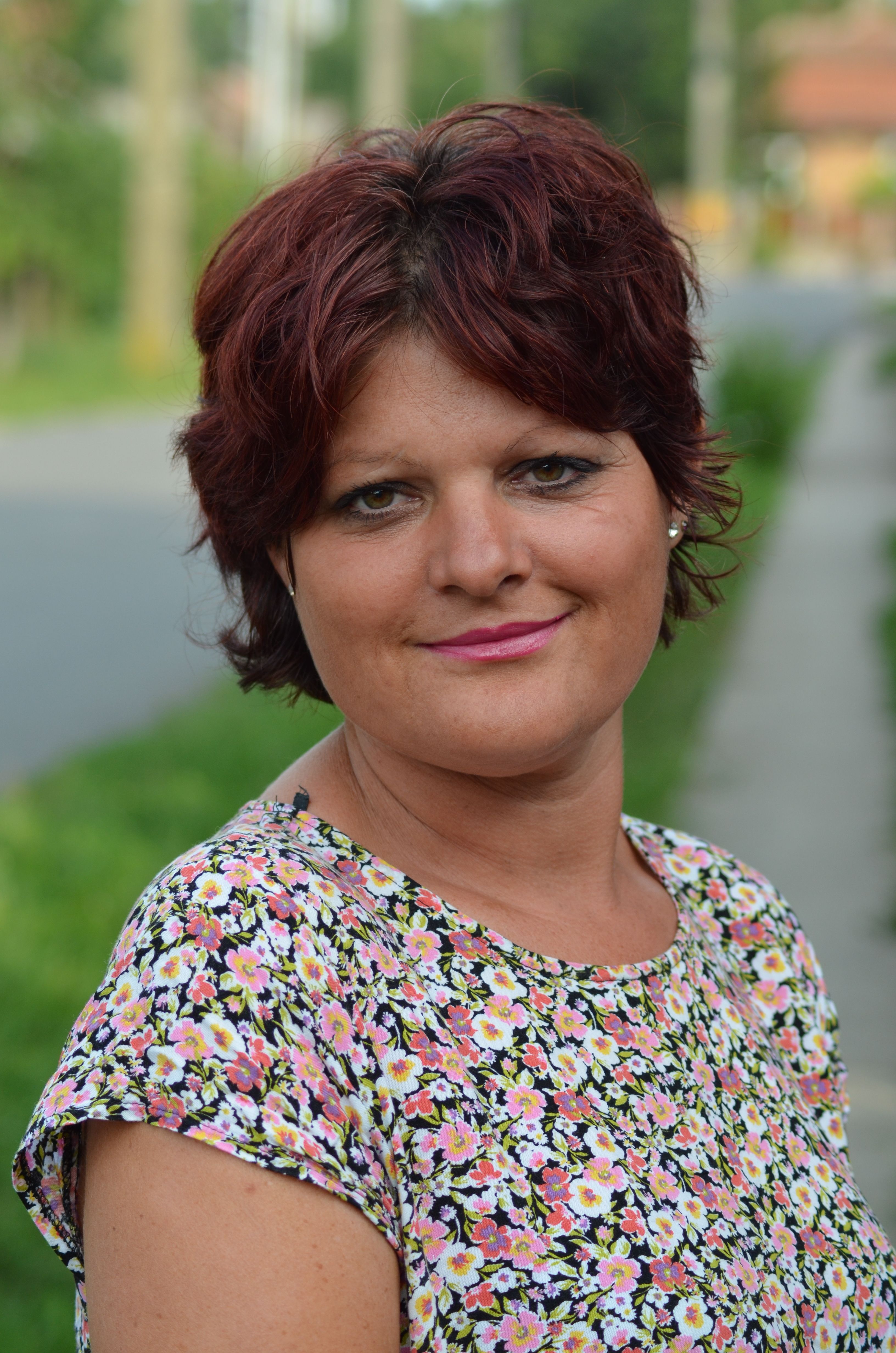 Portrait of a smiling woman with short hair wearing a floral top outdoors.