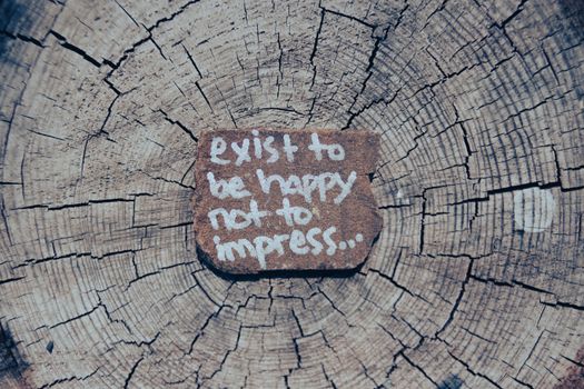 Motivational text on a piece of wood against a tree trunk background.