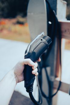 Close-up of a hand holding an EV charging cable outdoors, highlighting modern technology.