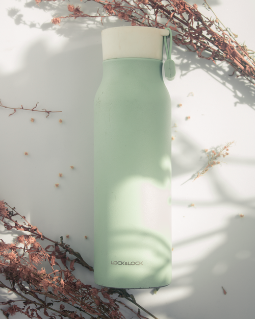 Free Minimalist water bottle surrounded by dried flowers, creating a serene aesthetic in soft light. Stock Photo