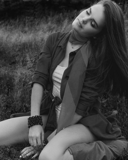 Free Black and white portrait of a woman posing elegantly outdoors on grass, showcasing a serene mood. Stock Photo
