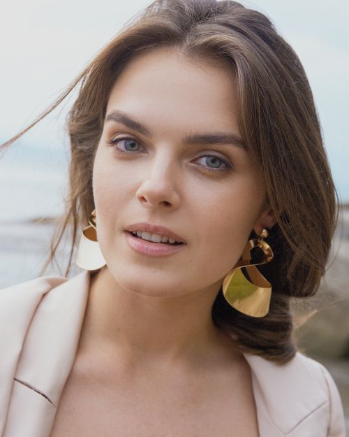 Free Close-up portrait of a woman wearing large gold earrings, set against a serene seaside background. Stock Photo