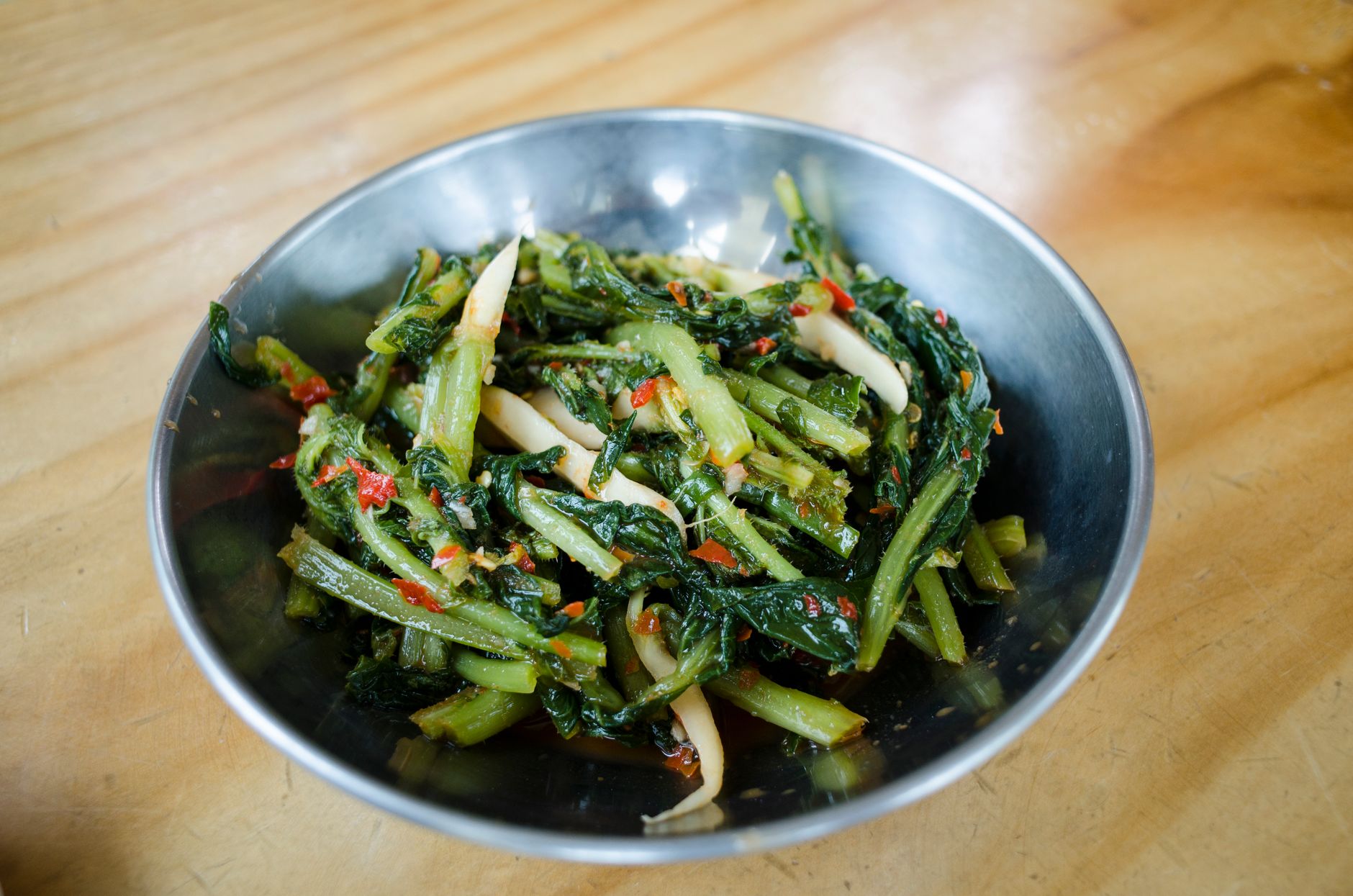 Delicious spicy Asian vegetable stir fry with red chili in a rustic metal bowl on a wooden surface.