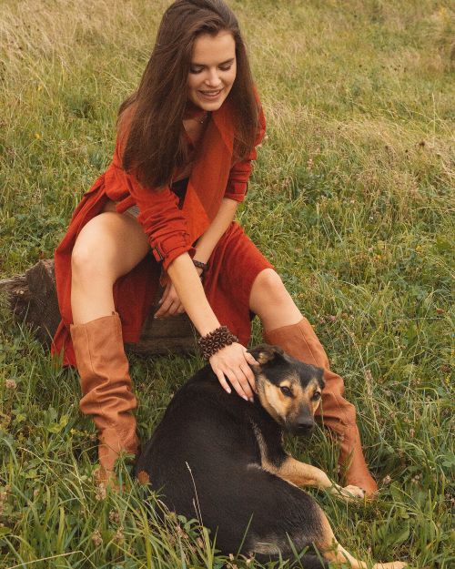 Free A woman in a bohemian outfit pets a dog on a grassy field on a sunny day. Stock Photo