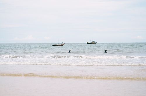 Free Calm ocean scene with boats and swimmers on a serene seashore. Stock Photo
