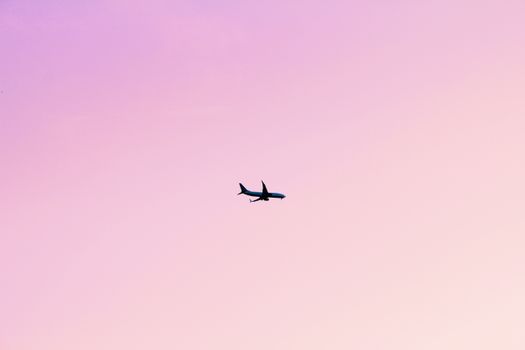 Airplane silhouette in flight across a serene pink sunset sky, minimalistic composition.