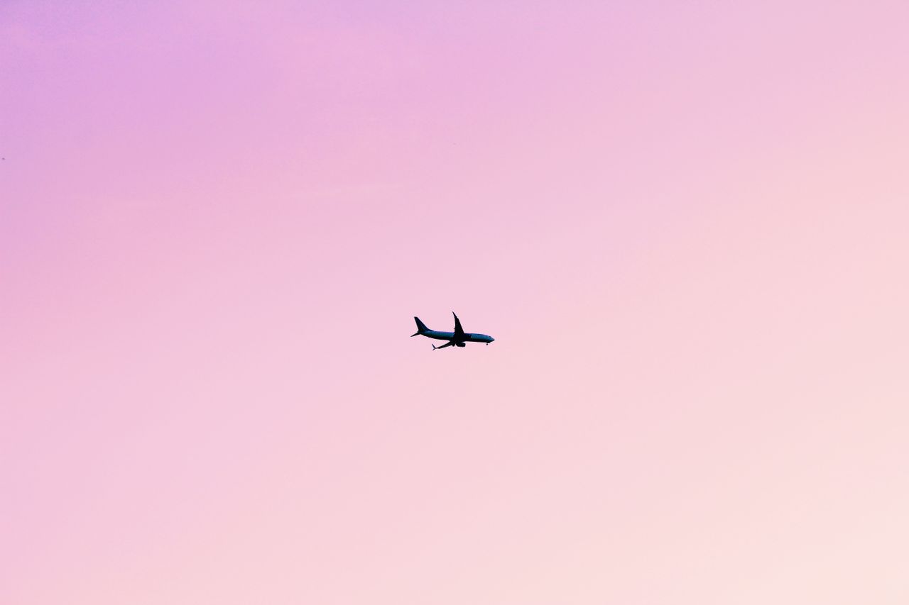 airplane silhouette in flight across a serene pink sunset sky minimali