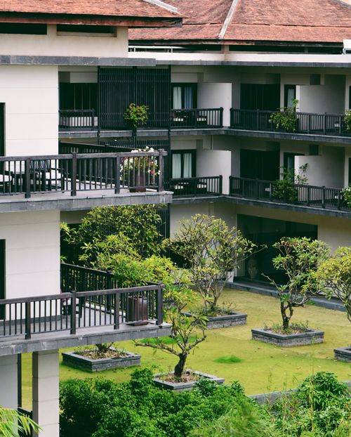 Free Contemporary multi-story building with lush courtyard and distinctive balconies, showcasing modern architecture. Stock Photo