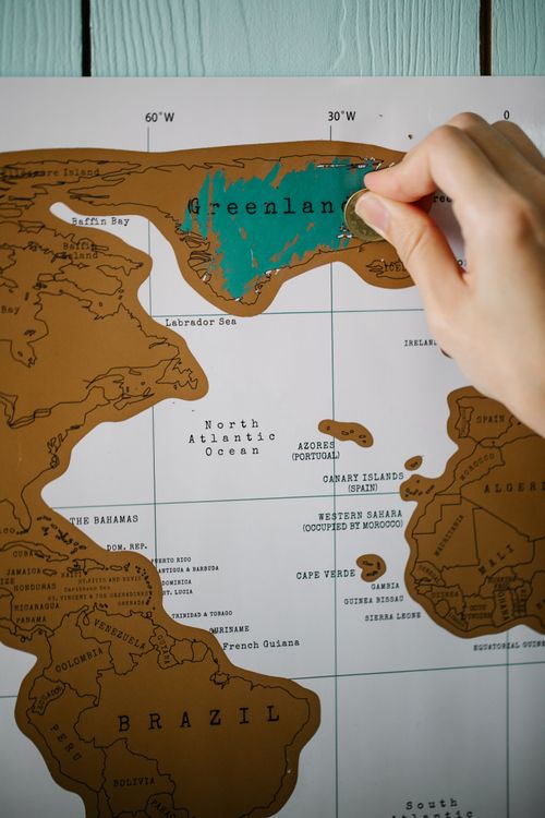 Free Close-up of a hand scratching a world map to reveal Greenland. Stock Photo