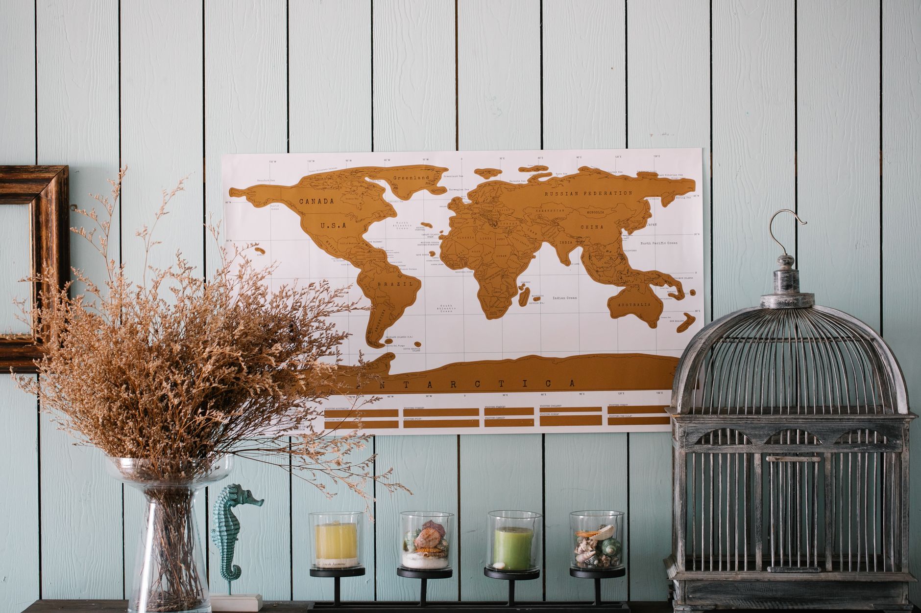 Elegant home decor featuring a world map, dried flowers, and vintage cage on a wooden wall.