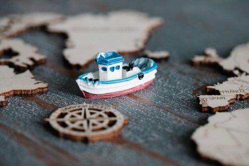 Free A close-up of a toy boat on a wooden map with a compass, representing travel and navigation. Stock Photo