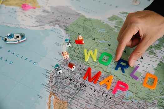Close-up of a hand placing colorful letters on a world map, highlighting the USA.