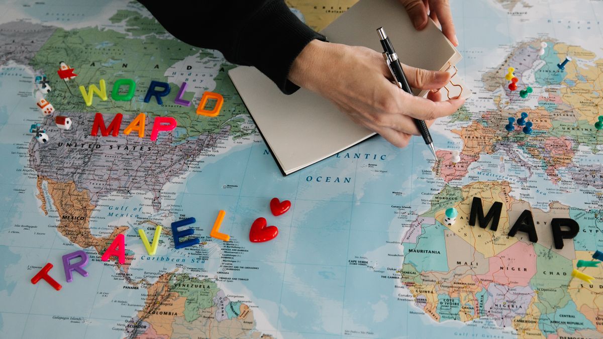 Hands holding pen and notebook over vibrant world map planning a journey.