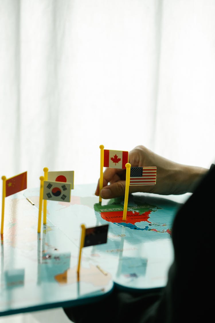 Hand Placing Small Country Flags On A Map