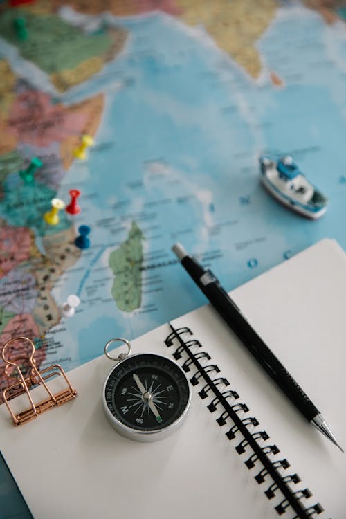 Mechanical Pencil, a Note Pad and a Navigational Compass Lying on a World Map