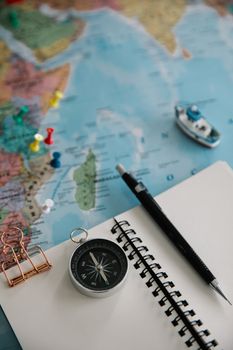 Flat lay of travel essentials including a navigational compass, pencil, notepad, and map for trip planning.