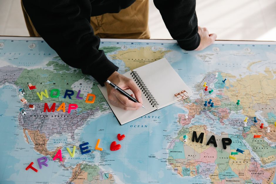 Person writing in a notebook laid open on a world map — most Americans travel internationally to access ibogaine treatment, with Canada and Mexico as the primary destinations