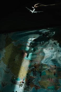 A model airplane held over a world map with dramatic lighting casting shadows.