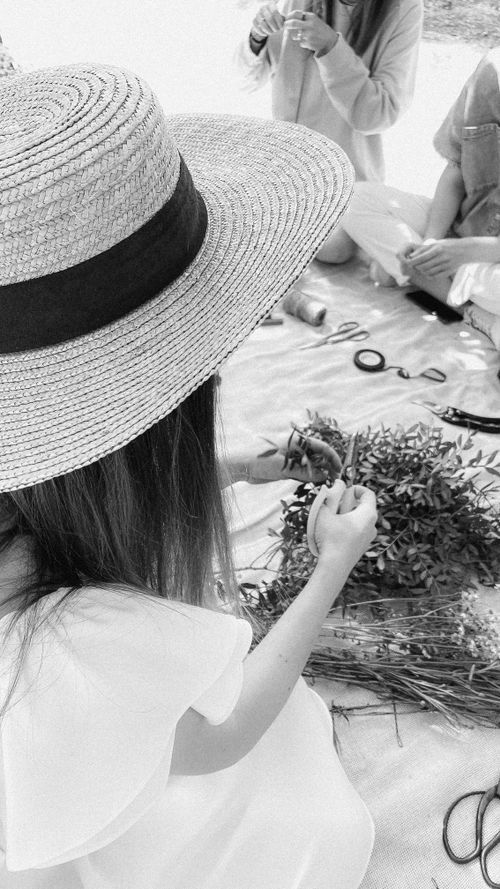 Free A woman crafting with floral materials, wearing a straw hat in a monochrome setting. Stock Photo