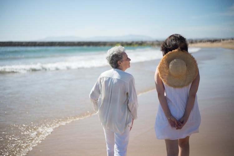 Mother And Daughter Walking On Beach Sand