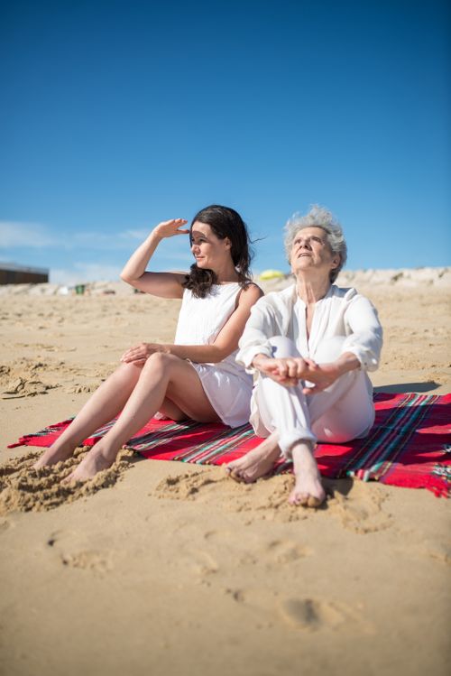 Free A mother and daughter enjoy a sunny day at a Portuguese beach, seated on a picnic blanket. Stock Photo