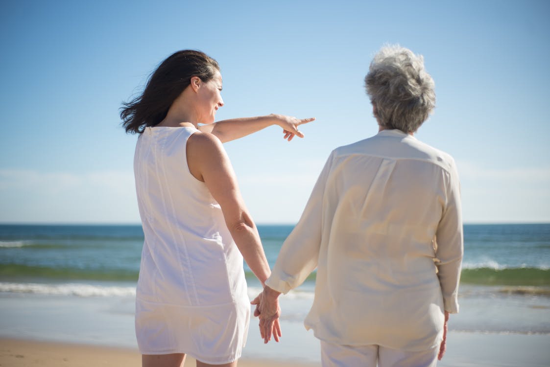 Free Woman Pointing at the Sea While Holding the Hand of an Elderly Woman Stock Photo