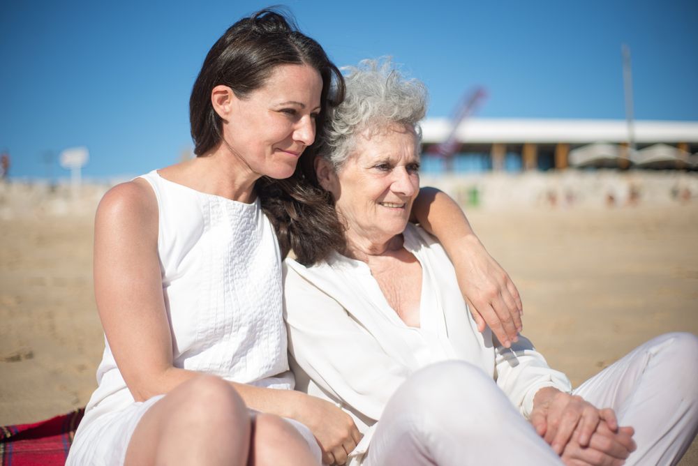 A daughter with her arm around her gray-haired mother on a sunny beach