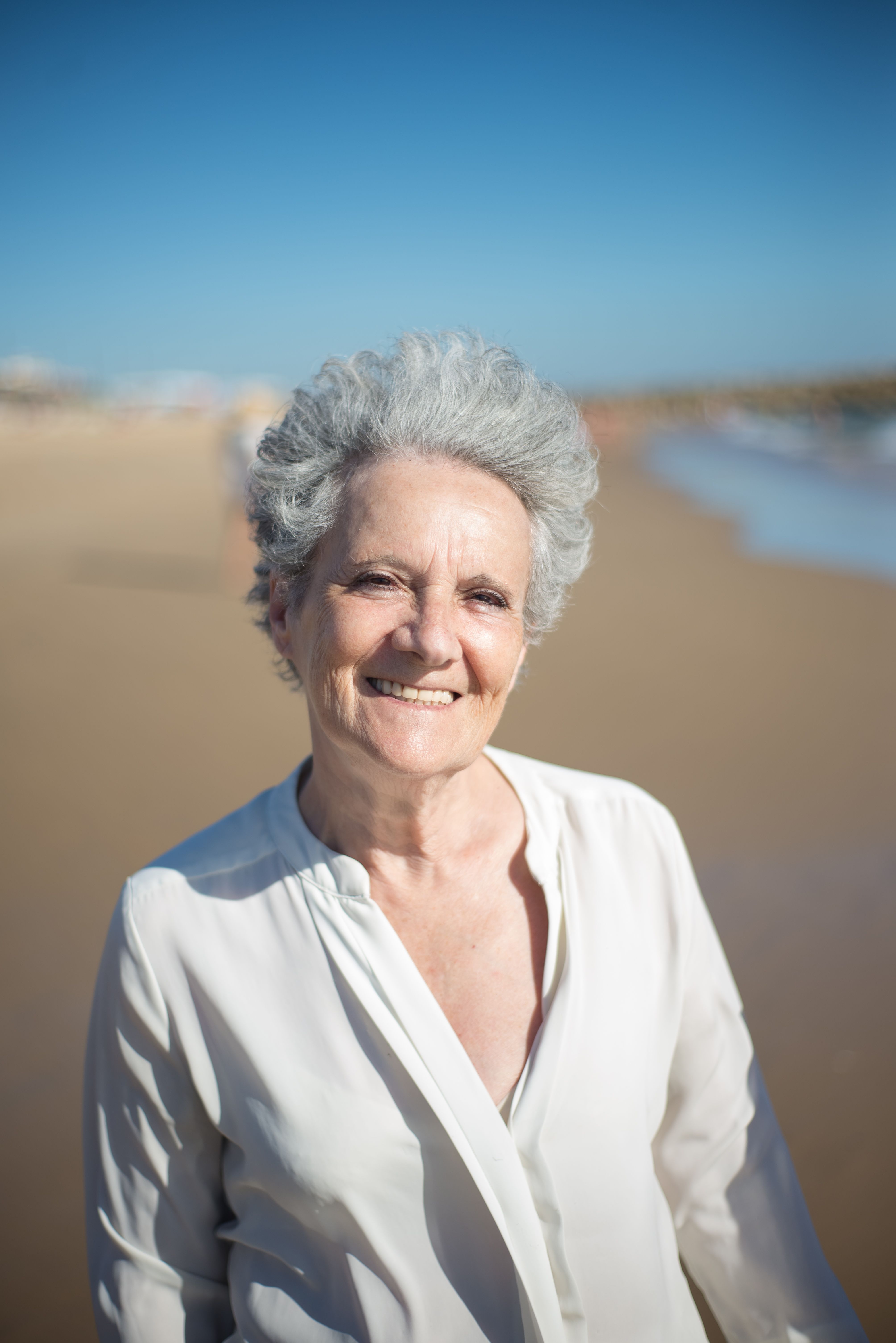 Senior woman with gray hair smiling brightly on a sunny beach in Portugal.