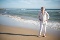 戴着耳机的高级女士在阳光明媚的葡萄牙海滩上欣赏音乐