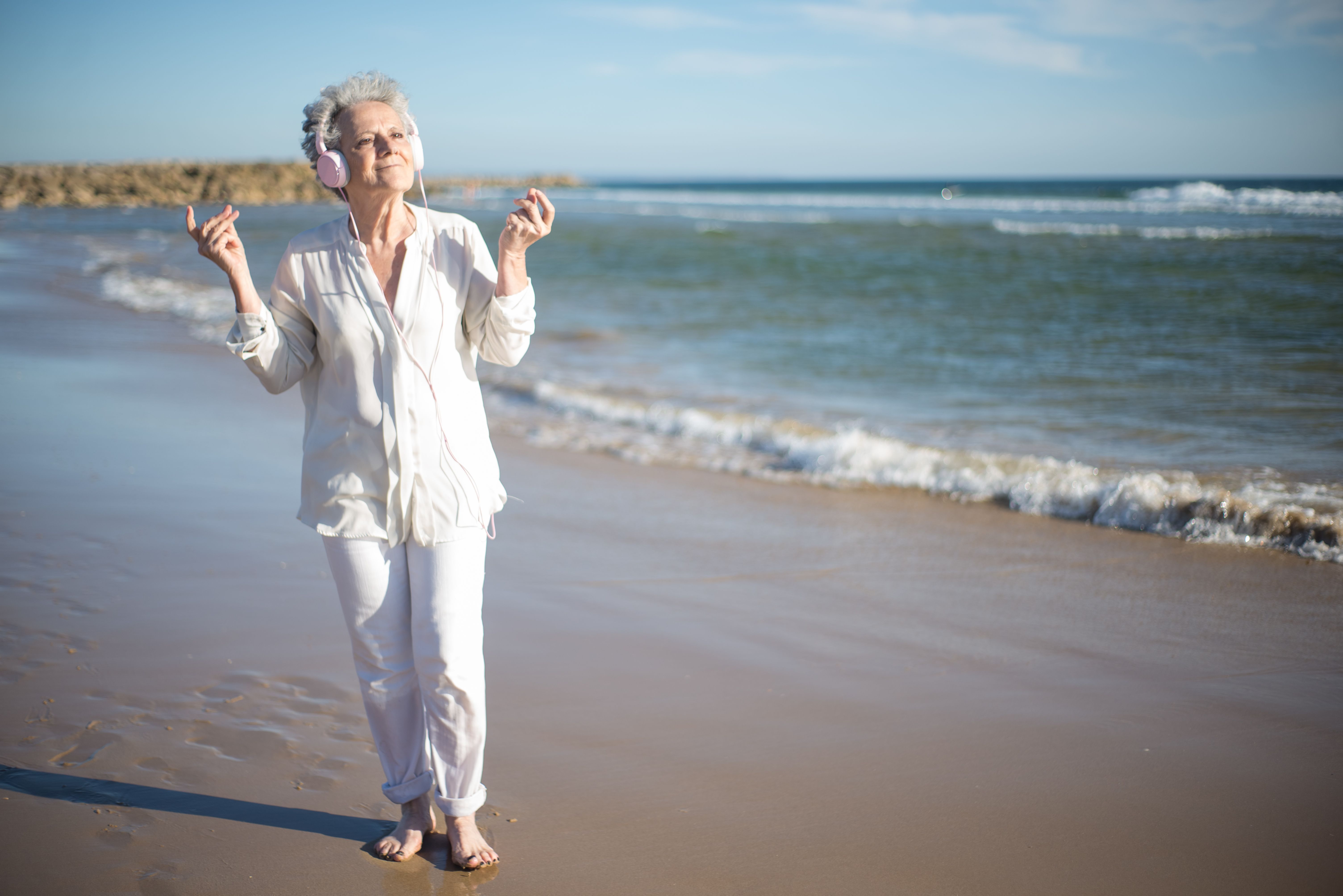 Senior woman with headphones enjoying music on a sunny beach in Portugal.