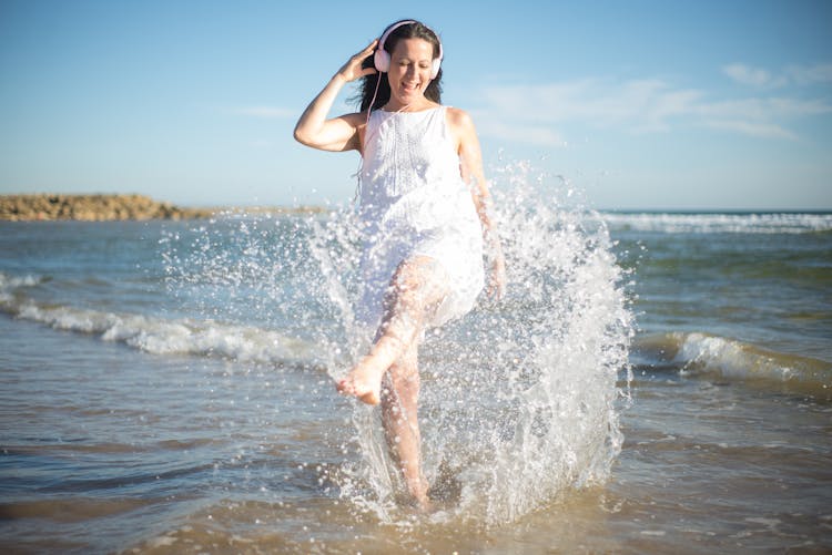 Woman With Headphones On Walking In The Sea And Splashing Water 