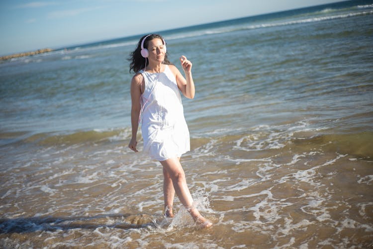 Woman In White Dress Walking On The Beach Wearing Headphones