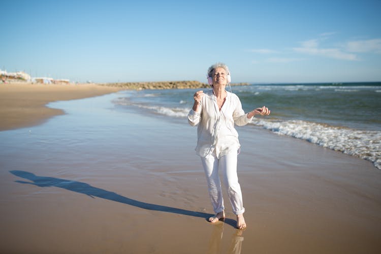 Elderly Woman Walking On The Beach Listening Music