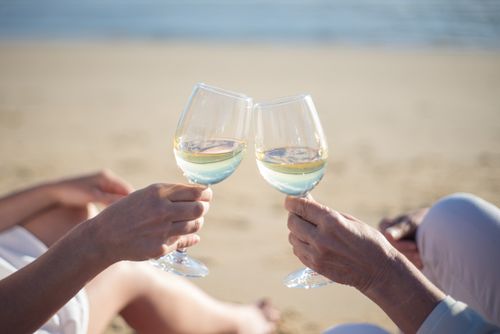 Free Close-up of two people toasting wine glasses on a sunny beach in Portugal. Stock Photo