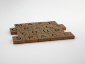 Wooden Scrabble tiles form the message "Make Grace Your Space" on a white surface.