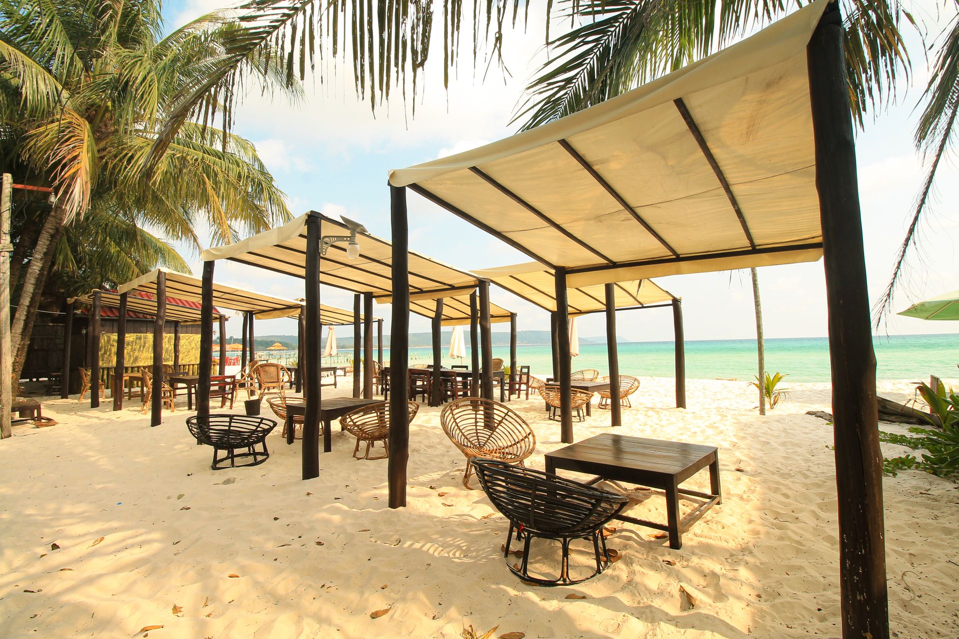 Scenic beachfront with canopies and chairs under palm trees for relaxation.