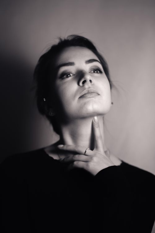 Free Elegant black and white portrait of a woman looking pensive with hand on neck in dramatic light. Stock Photo