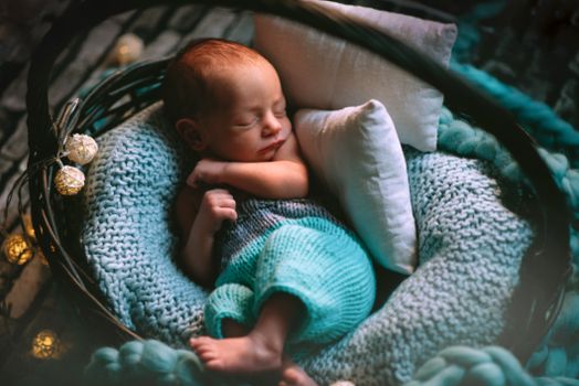 A peaceful newborn baby sleeping in a blue knitted basket, wrapped warmly with soft lighting.