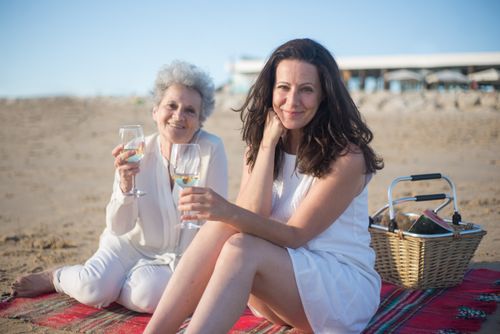 Free Two women enjoying a serene beach picnic with wine in Portugal, reflecting a joyful moment. Stock Photo