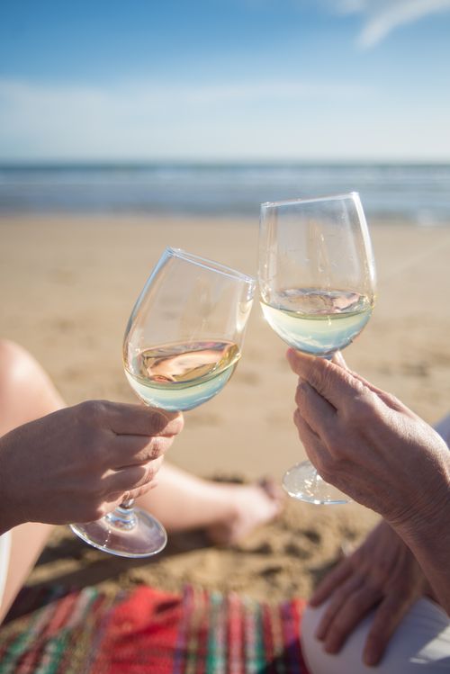 Free Close-up of two hands toasting wine glasses on a sunny beach in Portugal. Stock Photo