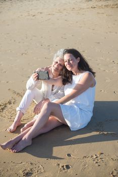 A joyful moment captured on the beach as a mother and daughter take a selfie together.