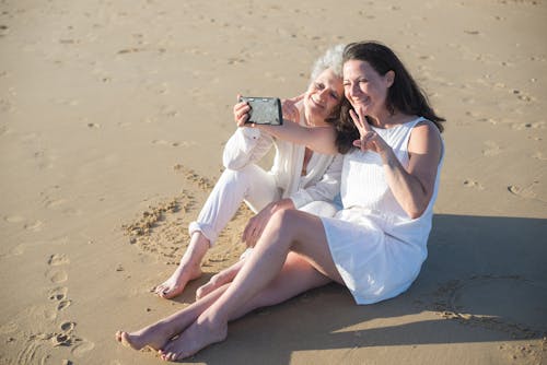 Women Sitting on Sand While Taking Selfie