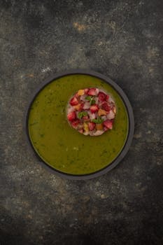 Appetizing green vegetable soup topped with fresh strawberries and herbs.